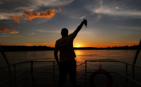 Silhouette of Wildlife photographer Clement Kiragu holding up a cocktail glass on a boat on the Zambezi river in Zambia